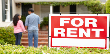 A couple standing outside of a house with a for-rent sign