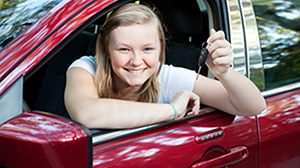 Teenage girl sitting in the drivers seat of a red car holding up her car keys