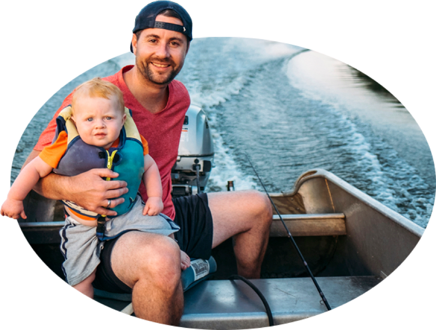 A bearded young father and his life-jacket-wearing toddler motor across the water in a fishing boat, one of the many types covered by State Farm boat insurance.