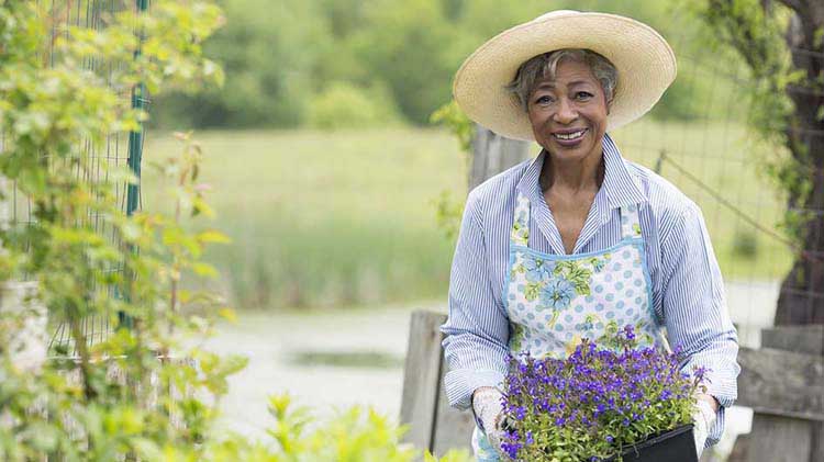 Woman in hat holding plants in garden