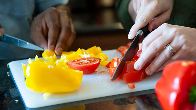 A couple is cutting organic peppers and tomatoes.