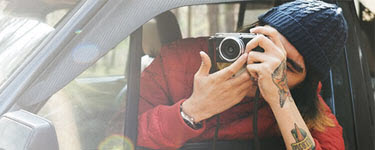 Man hanging out car window taking a picture with a camera