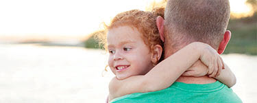 Girl in Dad's arms by rural lake
