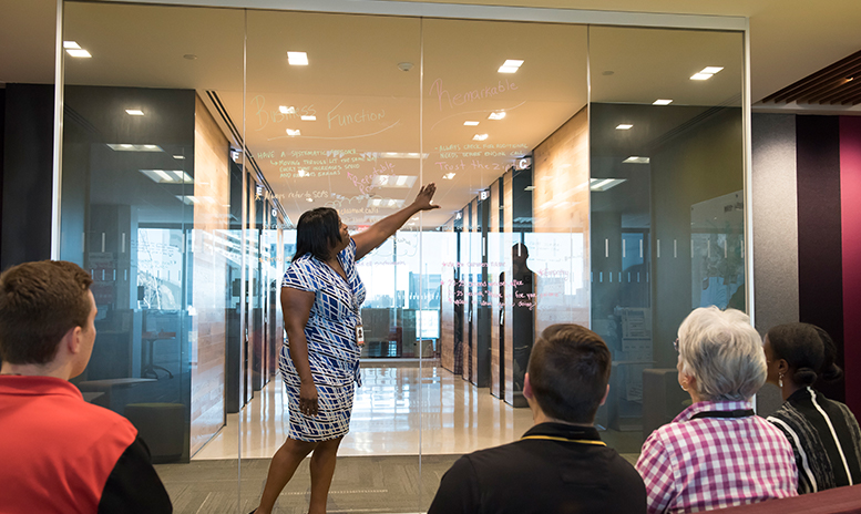 People in a meeting looking at a clear projected write board