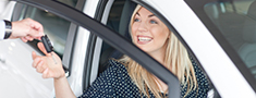 Young woman sitting in new car with key in showroom