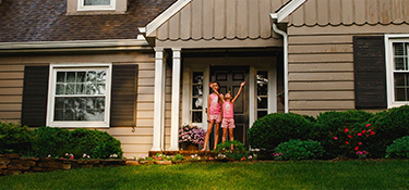 Two girls standing on the front porch of their house framed by a rainbow