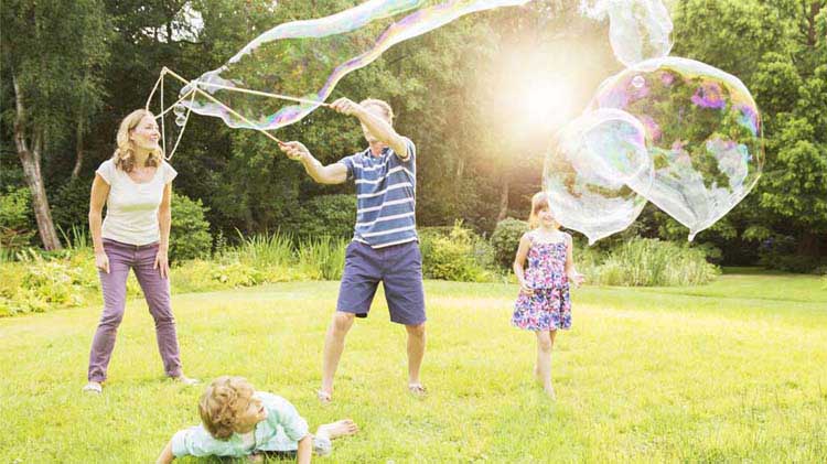 Family playing with giant soap bubbles in a yard