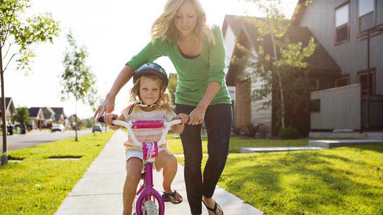 Mom helping young daughter learn to ride her bike