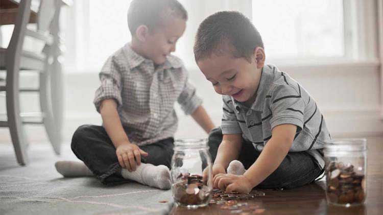 Two little boys are sitting on the floor protecting their finances by placing the coins in jars.