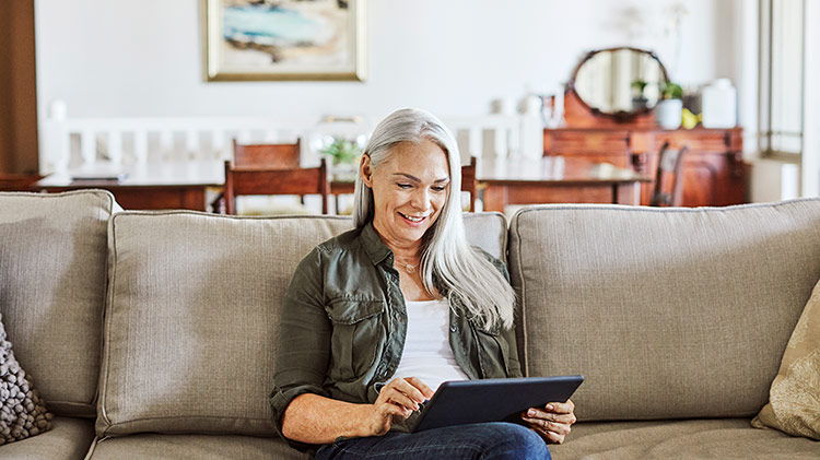 Older woman working on tablet computer on couch at home