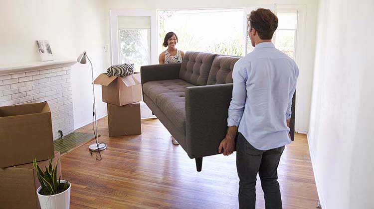 Una pareja cargando un sofa dentro de la casa nueva.