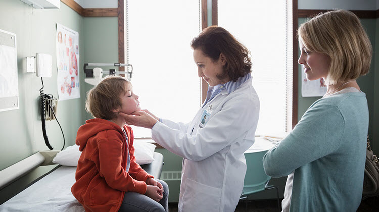 Doctor examining young child with mother watching