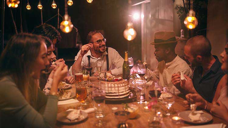 Guests at a house party are sitting around the table eating and talking