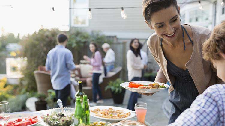 A woman at a house party is holding a plate of food while talking with another guest