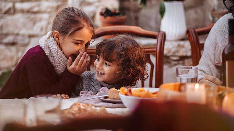 A little girl is whispering to another child while at a house party