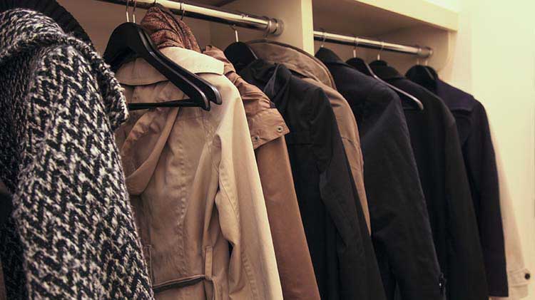 Coats are seen hanging in a closet while guests attend a house party