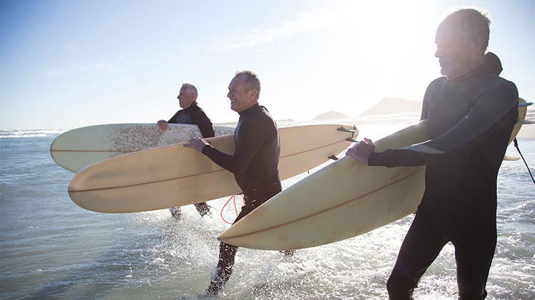 Tres hombres jubilados entran al océano para surfear.